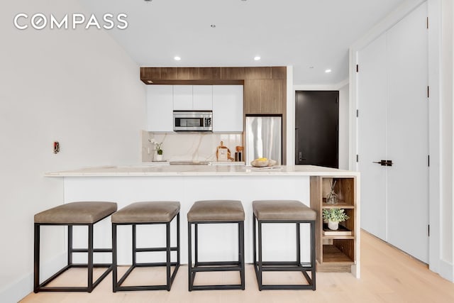 156 Somers St Unit 3B, New York City, NY 11233 - kitchen featuring appliances with stainless steel finishes, a breakfast bar, white cabinets, light countertops, and recessed lighting