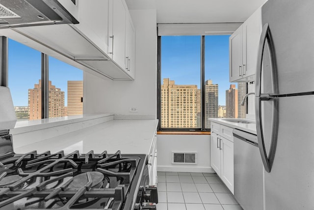 kitchen with appliances with stainless steel finishes, a sink, a skyline view, light tile patterned floors, and white cabinetry
