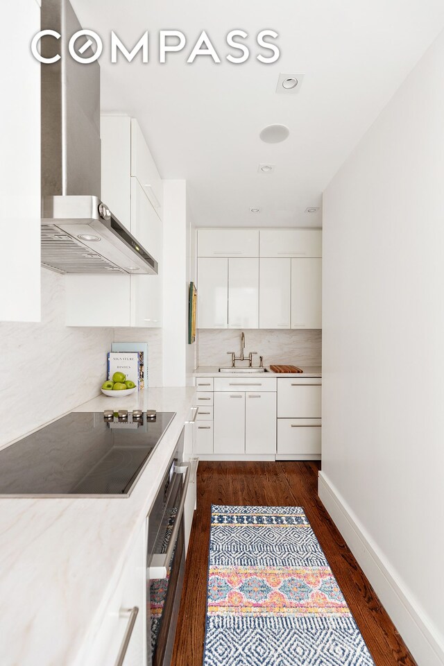 575 Park Ave Unit 1201, New York City, NY 10065 - kitchen featuring oven, black electric stovetop, wall chimney range hood, tasteful backsplash, and dark wood finished floors