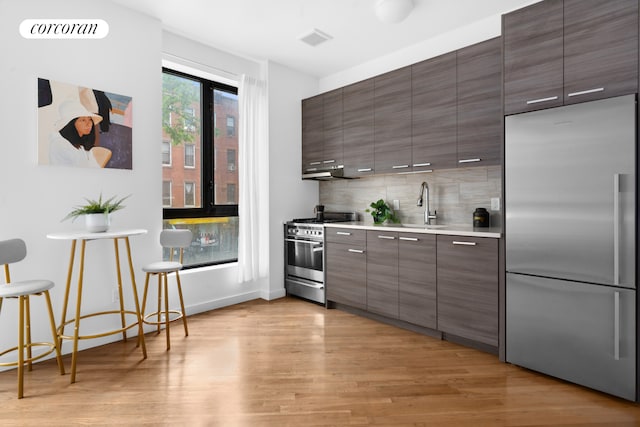 186 Putnam Ave Unit 2B, New York City, NY 11216 - kitchen with high end appliances, light wood-style flooring, decorative backsplash, light countertops, and under cabinet range hood
