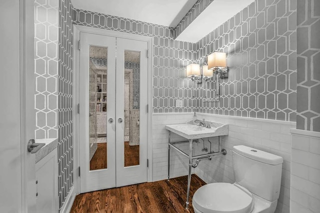 bathroom featuring french doors, wood finished floors, toilet, tile walls, and a sink