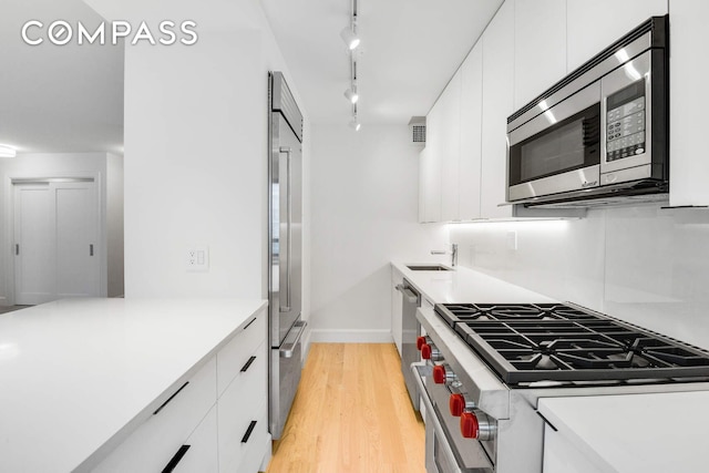 170 W End Ave Unit 12B, New York City, NY 10023 - kitchen featuring premium appliances, a sink, white cabinetry, track lighting, and light wood-style floors