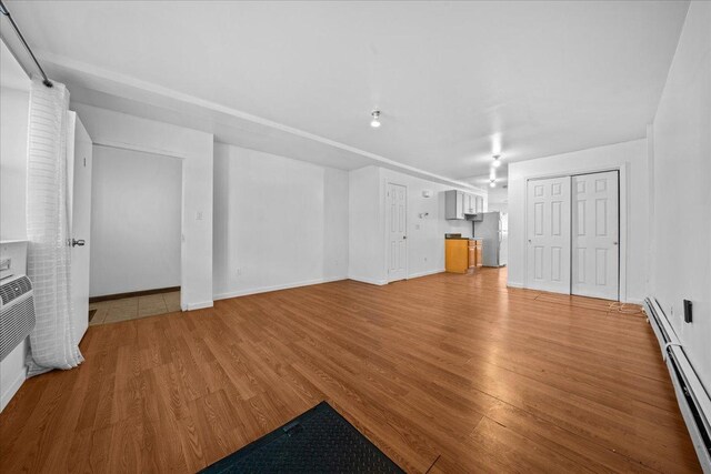 53 Woods Place, New York City, NY 11226 - unfurnished living room with light wood-type flooring, a baseboard heating unit, and baseboards