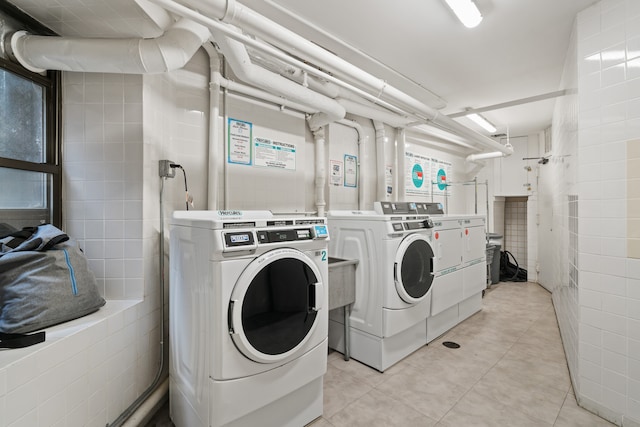 shared laundry room with washer and clothes dryer, light tile patterned flooring, and tile walls