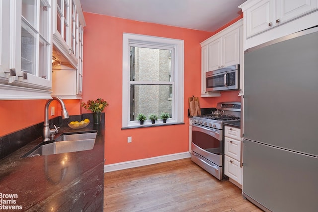 360 Riverside Dr Unit 8A, New York City, NY 10025 - kitchen featuring stainless steel appliances, white cabinetry, light wood finished floors, dark stone countertops, and glass insert cabinets