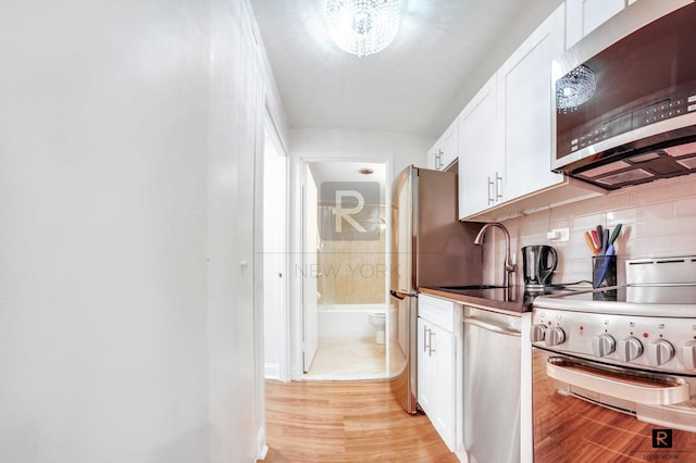 kitchen with stainless steel appliances, a sink, white cabinets, tasteful backsplash, and light wood-style flooring