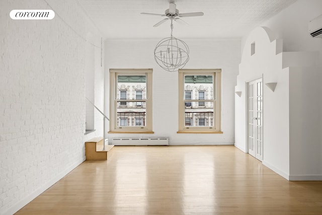 unfurnished dining area with baseboard heating, wood finished floors, a chandelier, ceiling fan, and brick wall