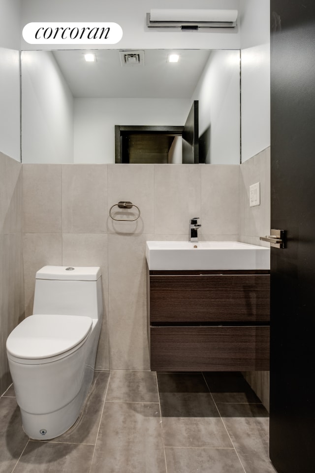 half bath featuring toilet, vanity, tile walls, and tile patterned floors