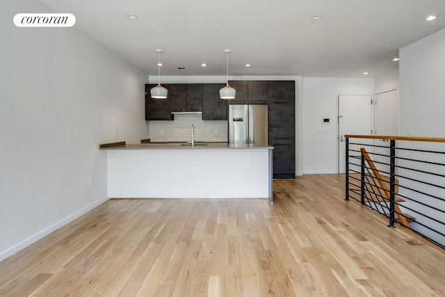 kitchen with stainless steel fridge, decorative backsplash, a peninsula, a sink, and light wood-style flooring