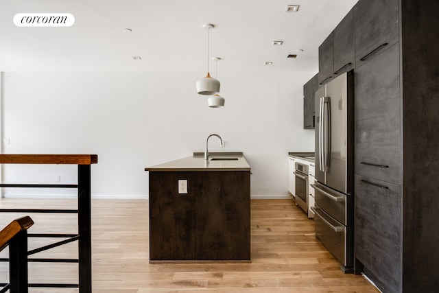 kitchen featuring a sink, stainless steel appliances, a center island with sink, light wood-style flooring, and pendant lighting