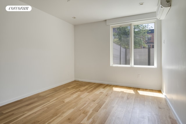 unfurnished room featuring a wall mounted air conditioner, light wood finished floors, and baseboards