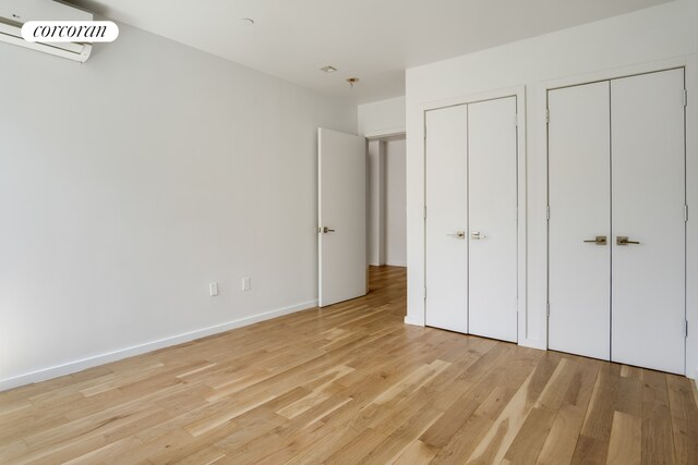 unfurnished bedroom featuring an AC wall unit, light wood-style flooring, multiple closets, and baseboards