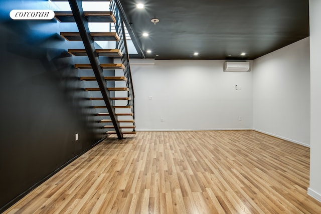 basement featuring a wall unit AC, wood finished floors, stairway, recessed lighting, and baseboards