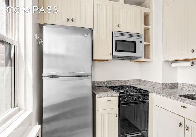 310 E 49th St Unit 7B, New York City, NY 10017 - kitchen with freestanding refrigerator, white microwave, black range with gas stovetop, open shelves, and light stone counters