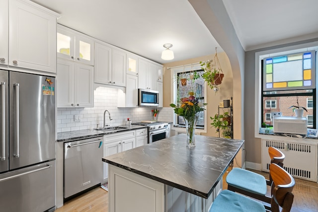 kitchen featuring premium appliances, radiator heating unit, a sink, tasteful backsplash, and white cabinetry