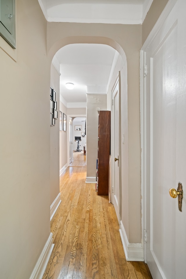 hallway with arched walkways, light wood-style floors, crown molding, and baseboards