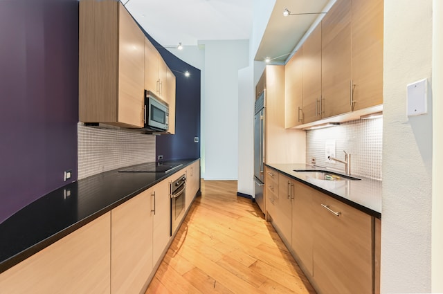 kitchen featuring stainless steel appliances, a sink, light wood-style flooring, and dark countertops