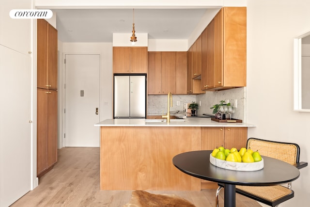 kitchen featuring built in fridge, a peninsula, a sink, light countertops, and tasteful backsplash