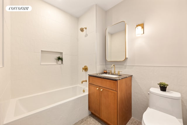 full bath with tiled shower / bath combo, toilet, vanity, a wainscoted wall, and tile walls