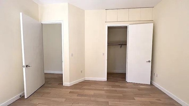 75 Wall St Unit 18Fg, New York City, NY 10005 - unfurnished bedroom featuring light wood-type flooring, a closet, and baseboards