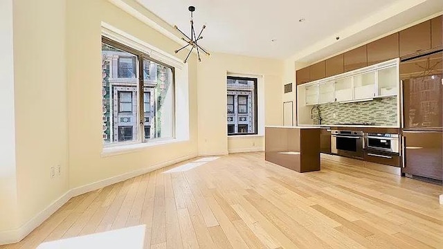 75 Wall St Unit 18Fg, New York City, NY 10005 - kitchen featuring oven, a chandelier, light wood finished floors, and decorative backsplash
