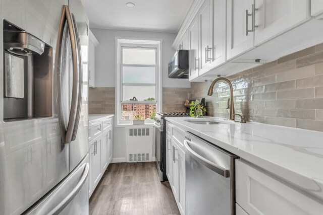 88-01 35th Ave Unit 5F, New York City, NY 11372 - kitchen with appliances with stainless steel finishes, radiator heating unit, a sink, white cabinets, and wood finished floors