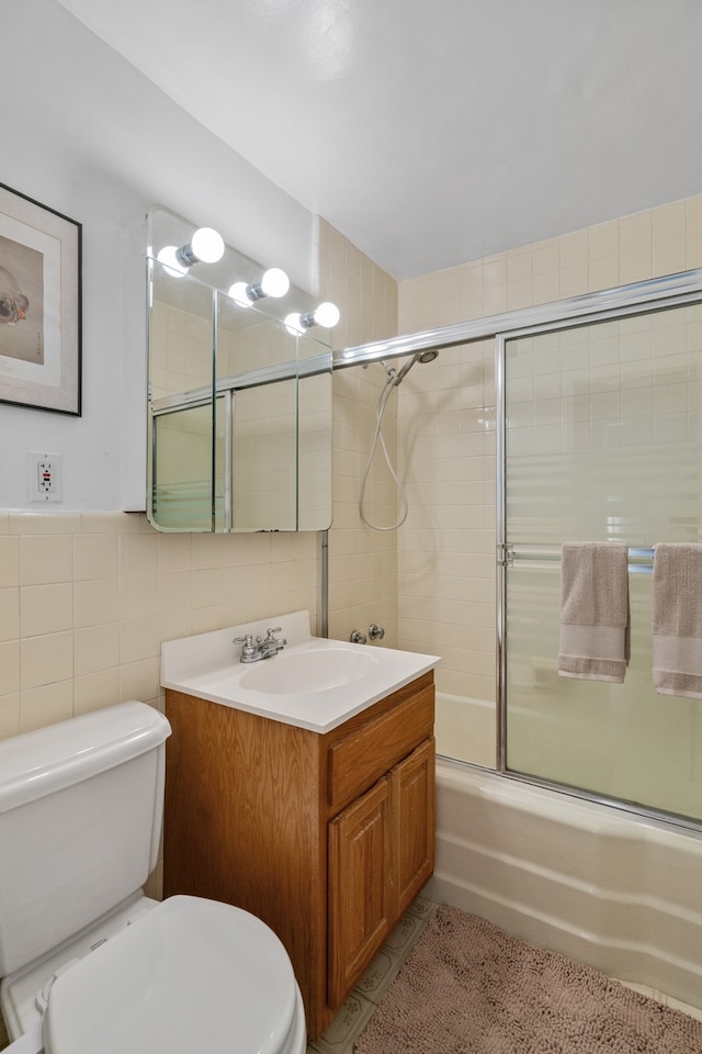 bathroom with tile walls, toilet, vanity, bath / shower combo with glass door, and tile patterned flooring