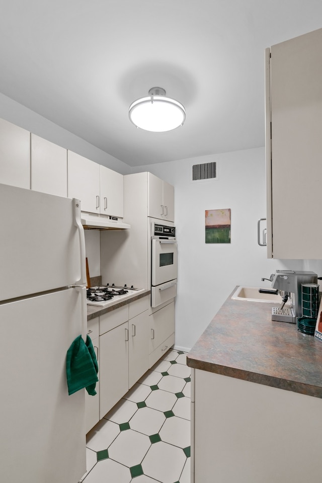 kitchen featuring white appliances, light flooring, under cabinet range hood, a sink, and a warming drawer