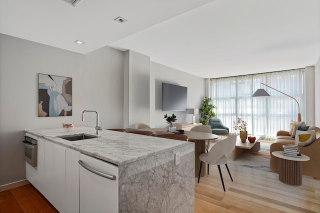 kitchen with a sink, light wood finished floors, light stone countertops, dishwashing machine, and oven