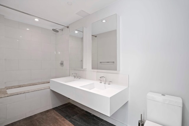bathroom featuring toilet, tiled shower, recessed lighting, and a sink