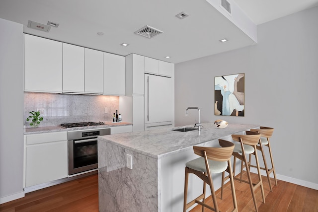 kitchen with appliances with stainless steel finishes, a sink, wood finished floors, a kitchen breakfast bar, and recessed lighting