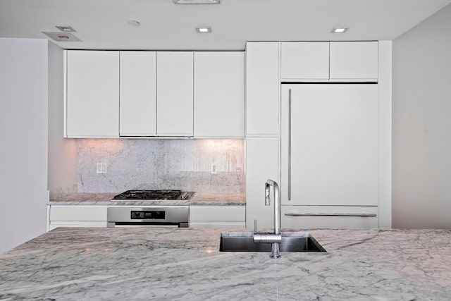 kitchen featuring oven, a sink, light stone countertops, white built in fridge, and white cabinets