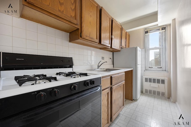 kitchen featuring gas range oven, radiator heating unit, a sink, brown cabinets, and tasteful backsplash