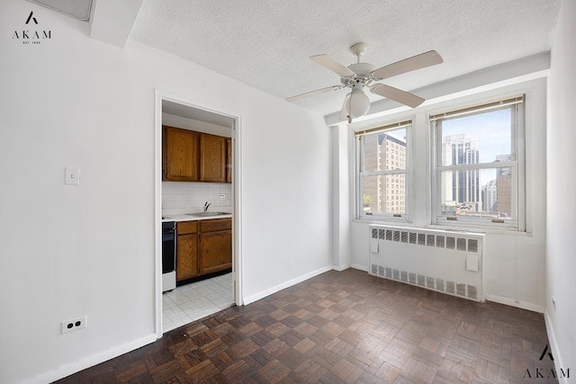 spare room featuring radiator heating unit, a sink, baseboards, a ceiling fan, and a textured ceiling