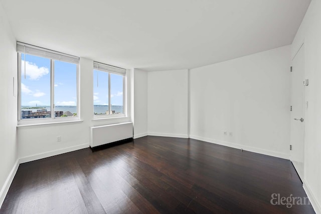 empty room featuring wood finished floors, radiator, and baseboards