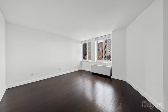 spare room with dark wood-style flooring and baseboards