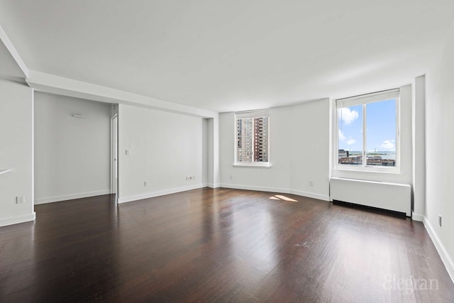 empty room featuring dark wood finished floors, baseboards, and radiator