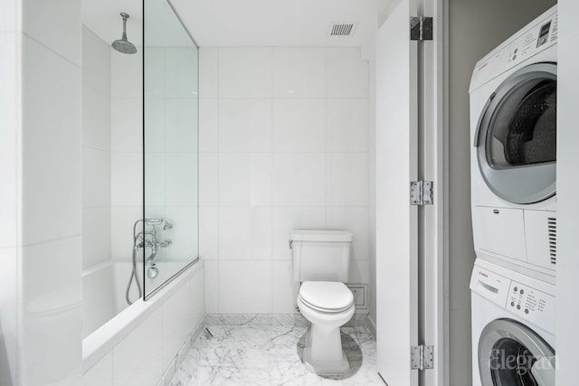 bathroom with stacked washer and clothes dryer, toilet, tile walls, and a combined bath / shower with rainfall shower