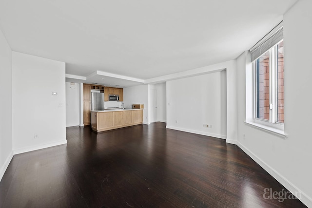 unfurnished living room with dark wood-style flooring, baseboards, and a sink