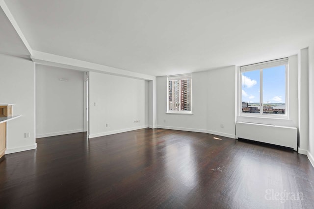 unfurnished living room with plenty of natural light, wood finished floors, radiator, and baseboards