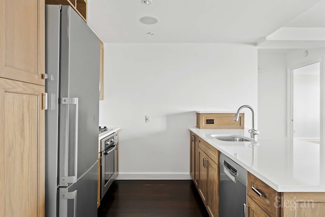 kitchen with appliances with stainless steel finishes, a sink, a peninsula, dark wood-type flooring, and baseboards