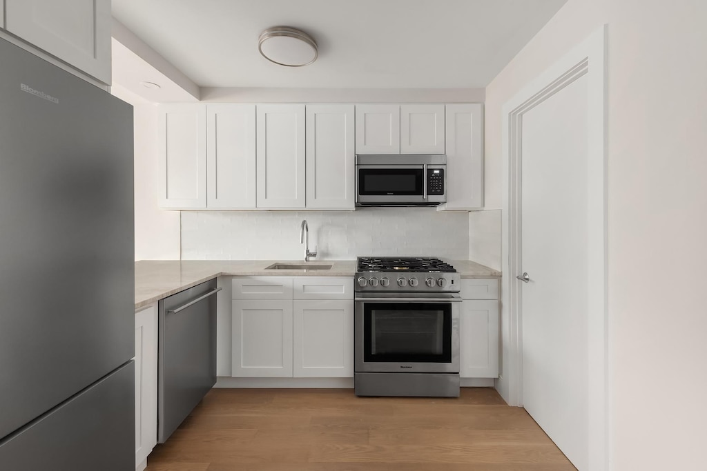 595 Main St Unit 814, New York City, NY 10044 - kitchen with stainless steel appliances, white cabinetry, light wood-style flooring, and light stone countertops