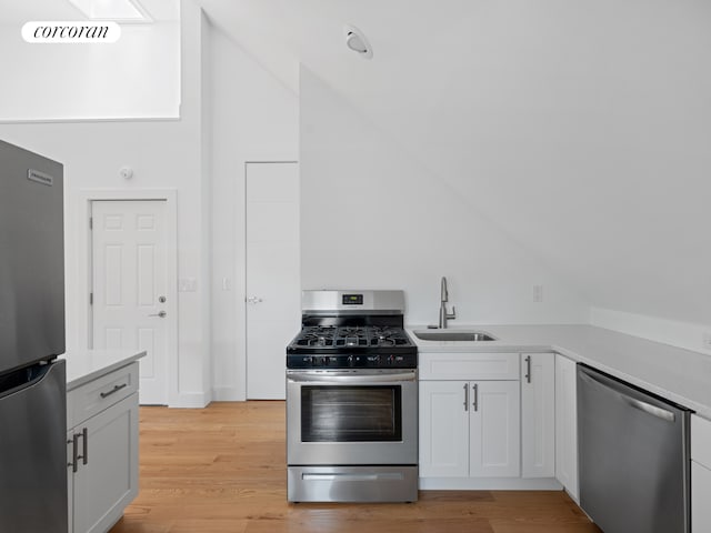kitchen with appliances with stainless steel finishes, vaulted ceiling, a sink, light countertops, and white cabinets