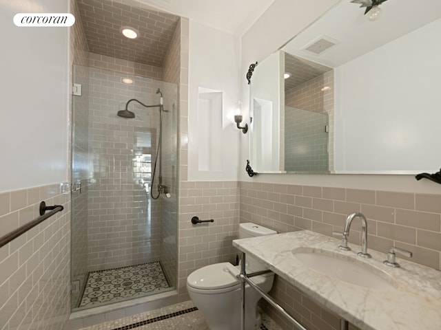 bathroom featuring tile walls, a sink, a shower stall, toilet, and wainscoting