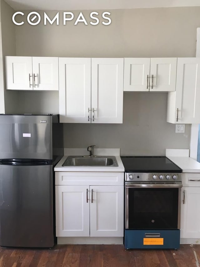 kitchen with appliances with stainless steel finishes, a sink, white cabinetry, and dark wood-style floors