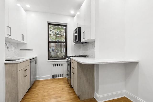 kitchen featuring a sink, stainless steel appliances, light wood finished floors, backsplash, and recessed lighting