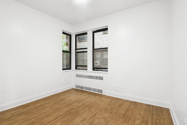 unfurnished room with radiator, baseboards, and wood finished floors