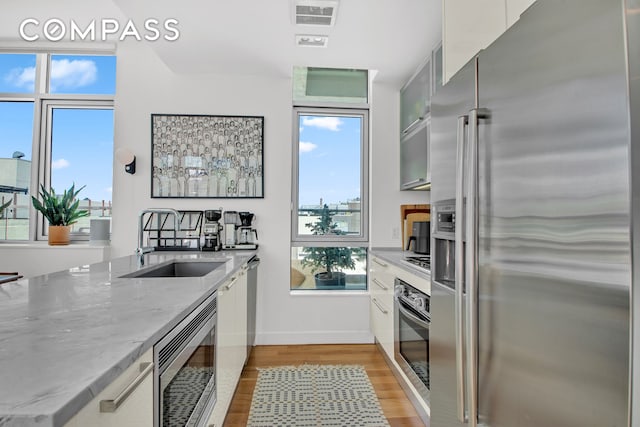 kitchen with appliances with stainless steel finishes, a sink, light wood-type flooring, baseboards, and light stone counters
