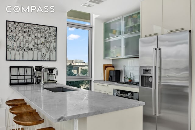 kitchen featuring appliances with stainless steel finishes, a sink, healthy amount of natural light, light stone countertops, and expansive windows