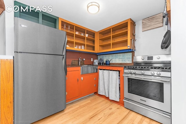 kitchen featuring appliances with stainless steel finishes, light wood-type flooring, dark countertops, and a sink